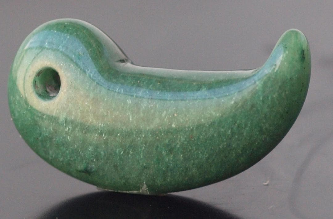 光にかざすと薄緑の細い帯状紋が出現、頭・胴の間には沈線、ずんぐり形の勾玉　沖縄の